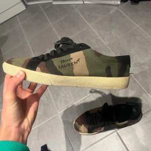Saint Laurent sneakers i camo - Saint laurent camo skor. Skorna är relativt bra skick utöver att limmet på sulan börjar gå upp.👏Borde däremot gå att lösa hemma eller hos en skomakare. Skorna är köpta på TheRealReal!  Inget OG tillkommer 