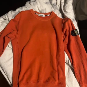 Stone island tröja äkta orange  - Säljer en snygg orange sweatshirt från Stone Island med klassisk patch på vänster ärm. Tröjan har rund hals, ribbade muddar och är tillverkad i mjuk bomull. Perfekt för dig som gillar streetwear och vill sticka ut med färg. Äkta 