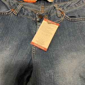 Dallas Jeans blå raka jeans W27 L33 - Snygga blå jeans från Dallas Jeans med klassisk femficksdesign och raka ben. Jeansen har orangea sömmar och en normal passform. Materialet är slitstarkt denim i bomull och färgen är ljusblå med lätt tvättad look.