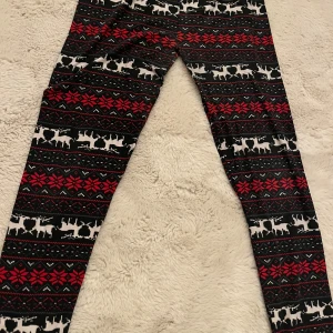Jätte sköna Svarta leggings med julmönster - Mysiga svarta leggings med rött och vitt julmönster, inklusive renar och snöflingor. Stretchig midja och mjukt material som är perfekt för chill hemma eller julmys. Snyggt mönster som sticker ut och ger vinterkänsla.
