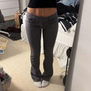 Grå bootcut byxor med låg midja - Snygga grå byxor med bootcut och låg midja. Byxorna har två knappar framtill. Materialet är mjukt och stretchigt, vilket gör dem bekväma att bära hela dagen. Perfekta för dig som gillar en stilren och trendig look.