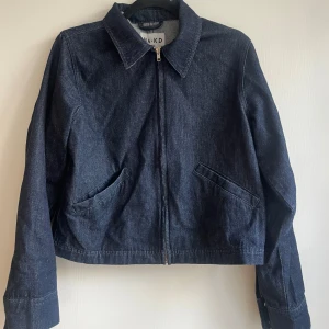 Mörkblå jeansjacka från NA-KD - Snygg mörkblå jeansjacka från NA-KD med klassisk krage och raka långa ärmar. Jackan har två snedställda fickor framtill och stängs med dragkedja. 