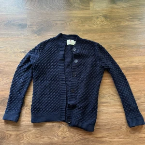 Stickad kofta - Mysig mörkblå stickad kofta från Ellos med grov struktur och ribbade muddar. Koftan har knappar framtill och lång ärm, perfekt för lager-på-lager-stil. Enkel att matcha med jeans eller kjol för en chill look.