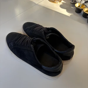 Svarta sneakers från Axel Arigato 43 - Svarta sneakers från Axel Arigato i mocka och detaljer i skinn. Klassisk låg modell med rund tå, snörning och vit platt gummisula. Storlek 43. Sparsamt använda