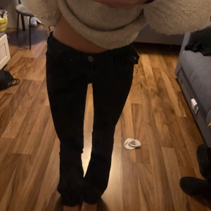 Svarta lågmidjade jeans true religion  - Säljer ett par svarta jeans från true religion med låg midja och klassisk femficksdesign. Jeansen är utsvängda och en snygg passform som sitter tajt över höfterna. Perfekta för dig som gillar en stilren och enkel look.
