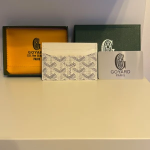 Vit G yard plånbok med mönster - Exklusiv vit plånbok från G med ikoniskt grafiskt mönster i grått. Slimmad design med flera kortfack, perfekt för dig som gillar stilrena accessoarer. Kommer med originalask och certifikat. Lyxig känsla och klassisk Paris-vibe.