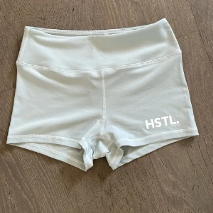 Ljusblåa träningsshorts från HSTL Made - Säljer ett par ljusblåa, högmidjade träningsshorts från HSTL Made. De är tighta och har en mjuk, stretchig känsla i syntetmaterial. Perfekta för gymmet eller andra sportiga aktiviteter. Diskret logga framtill och bred resår i midjan för extra komfort.