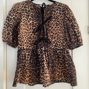 Leopardmönstrad blus med snörning - Säljer en blus med leopardmönster i bruna och svarta toner. Modellen har puffiga korta ärmar, volang nedtill och snygg snörning framtill. Perfekt för dig som vill sticka ut med ett djurmönster och coola detaljer. Mått Över bröstet: ca 45 cm Längd från axeln och ner: ca 61 cm  85% viskos och 15% nylon  Kommer från ett djur och rökfritt hem.