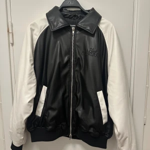 Svartvit bomberjacka från Cropp - Snygg svartvit bomberjacka från Cropp med broderad text 'Lost Dreamer' på ryggen. Jackan har svarta paneler och vita ärmar, dragkedja framtill och två fickor. Tillverkad i skinnimitation för en cool look.