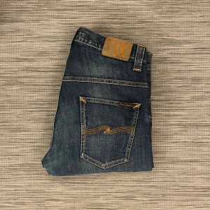 Nudie Jeans - Ett par riktigt fina jeans från Nudie i modellen ”Thin Finn”. De har använts sparsamt och har inga skador eller hål. Endast små tecken av användning såsom blekning i tyget.   W: 32 ~ 40cm L: 34 ~ 109cm Ankelvidd: ~ 19cm Lårvidd: ~ 26cm  Hör av er vid frågor eller funderingar!