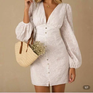 Vit kortklänning med puffärmar - Superfin vit kortklänning med v-ringning, puffiga långärmar och små blommiga broderier. Klänningen har knappar framtill och markerad midja som ger en snygg siluett. Perfekt för dig som gillar romantisk och feminin stil. Liknande adoore klänning!! Säljer då den inte kommer till användning 