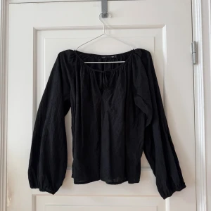 Svart blus med broderade detaljer 157 - Svart blus från 157 i storlek S, tillverkad i 100% bomull. Blusen har långa puffärmar, rundad hals med knyt och broderade blommor över hela tyget. Använd en gång.