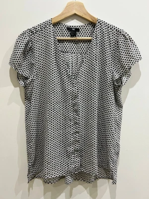 Mönstrad blus från H&M - Snygg blus från H&M i vitt med svart grafiskt mönster. Blusen har korta ärmar med lätt puff och knappar framtill. Tunt och luftigt material som ger en avslappnad känsla. Perfekt att matcha med jeans eller kjol.