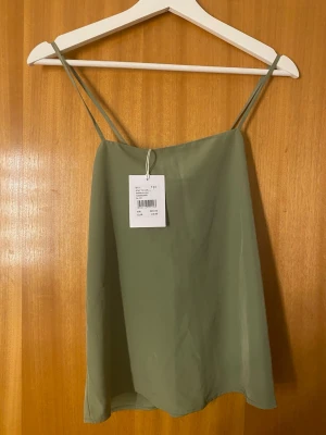 Olivgrön linnetopp med tunna band - Snygg olivgrön linnetopp från Stay To Cari med tunna axelband och enkel, rak passform. Helt oanvänd