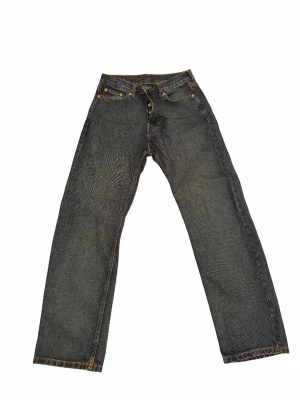 Svarta raka jeans  - Säljer ett par svarta jeans med raka ben och klassisk femficksmodell. Jeansen har kontrastsömmar i orange och en patch bak i midjan. Tillverkade i kraftigt denimtyg som ger en tidlös look.