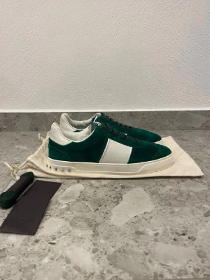 Gröna Valentino Flycrew skor  - Stilrena sneakers från Valentino i grön mocka med vita detaljer och vit sula. Klassisk låg modell med gröna skosnören och extra snören medföljer. Orginalbox tillkommer