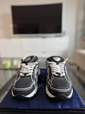 Svarta dior b30 sneakers  - Snygga svarta sneakers från Dior med vita kontrastdetaljer och vita snören. Skorna har en chunky sula och tydlig CD-logga på sidan samt Dior-märke på hälen. Ovandelen är i mesh och syntetmaterial för en sportig vibe.