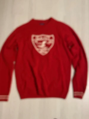Röd GANT tröja med skidmärke - Röd långärmad tröja från GANT med vitt broderat skidmärke och texten 'GANT 1949 NHCT' på bröstet. Tröjan har ribbade muddar med vita ränder vid ärmslut och nederkant. Perfekt för dig som gillar sportig och klassisk stil. Unik sitter som en smal.  Sjuk mjuk och gosigt material😁