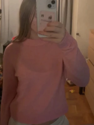 Rosa croppad stickad tröja - Säljer en söt rosa croppad stickad tröja med rund hals och långa ärmar. Tröjan har en enkel och clean design med ribbade muddar vid ärmslut och nederkant. Perfekt för dig som gillar en mjuk och avslappnad stil.