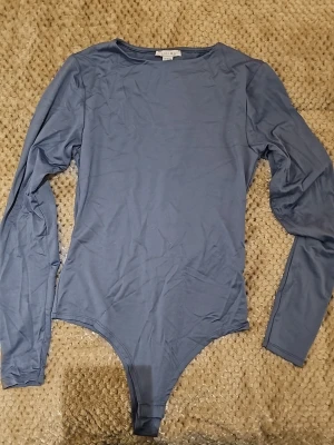 Blå långärmad body från Amisu - Snygg blå body från Amisu med långa ärmar och rund halsringning. Tillverkad i ett mjukt och stretchigt material som sitter skönt mot kroppen. Perfekt att styla med jeans eller kjol för en clean look.