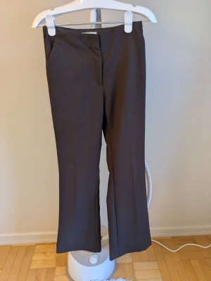 Bruna kostymbyxor med pressveck - Snygga bruna kostymbyxor med raka ben och pressveck framtill. Byxorna har diskreta fickor bak och stängs med hake och dragkedja. Perfekta för en clean och stilren look. Materialet känns mjukt och har lite stretch för extra komfort.