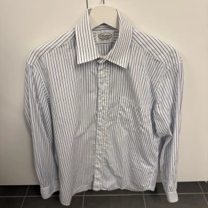 Randig skjorta från Stenströms - Klassisk vit skjorta från Stenströms med tunna blå ränder. Skjortan har lång ärm, bröstficka och knappar framtill. Tillverkad i bomull och har en tidlös, normal passform som funkar till många olika stilar.