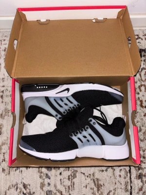 Nike Air Presto svart/vita sneakers - Nike Air Presto sneakers i svart mesh med vit plastdetaljer och vit sula. Skorna har en sportig look med klassisk Nike-logga på sidan och tungan.
