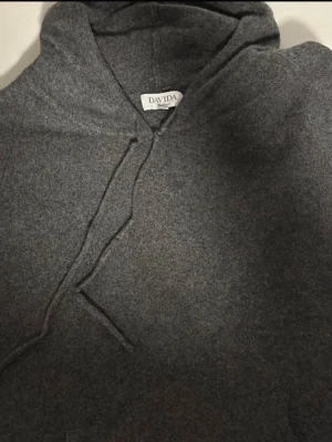  Davida Cashmere Hoodie - Mjuk och lyxig mörkgrå hoodie från Davida i 100% cashmere. Klassisk modell med huva och dragsko, perfekt för en chill och stilren look. Passar dig som vill ha något extra skönt och snyggt i garderoben. Står som storlek XL, men pga materialet som drar åt sig så passar den mer L/M