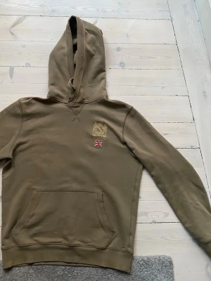 Olivgrön hoodie från Morris - Olivgrön hoodie från Morris med broderad guldfärgad logga och brittisk flagga på bröstet. Väldigt bra skick