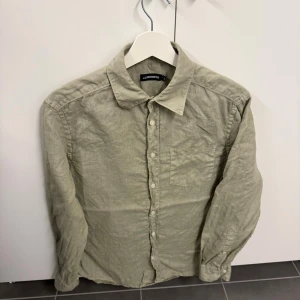 Grön linneskjorta från J.Lindeberg - Stilren grön skjorta från J.Lindeberg i svalt linnematerial. Klassisk krage, långärmad modell och bröstficka. Perfekt för dig som gillar en avslappnad men ändå snygg look.