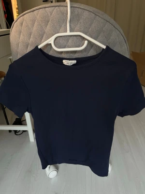 Mörkblå basic t-shirt från Gina Tricot - En stilren mörkblå t-shirt från Gina Tricot med klassisk rund halsringning och korta ärmar. Modellen är enkel och passar perfekt till jeans eller kjol. Tillverkad i mjuk bomull för en bekväm känsla hela dagen.