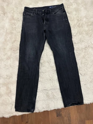 Svarta raka jeans G raw star - Säljer ett par svarta jeans från G raw star med rak passform och klassiska fem fickor. Jeansen har knappgylf och diskreta slitningar för en cool look. Perfekta till en avslappnad stil och funkar året runt.