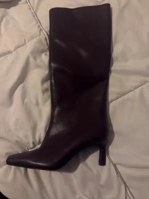 boots med klack - Snygga mörkbruna stövlar i skinn med spetsig tå och smal klack. Stövlarna har en stilren design och når upp till vaden, perfekta för att lyfta din outfit. använda ett tillfälle 
