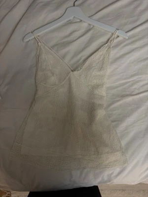 Vit spetslinne med tunna axelband - 2000s vibe - Säljer en söt vit linnetopp med spetsdetaljer och smala axelband. Toppen har v-ringning och är ärmlös, perfekt för varma dagar. Materialet är lätt och luftigt.