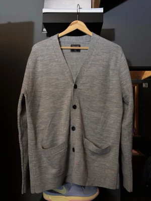 Grå kofta från Abercrombie & Fitch - Snygg grå kofta från Abercrombie & Fitcji mjuk ullmix. Klassisk design med v-ringning, knäppning framtill och två fickor. Perfekt för lager på lager och enkel att matcha med olika outfits.