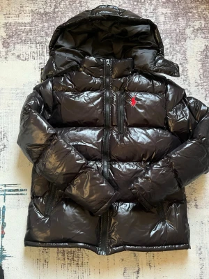 Svart glansig dunjacka med huva - Ralph lauren jacka , glansig. För mer detaljerade bilder kontakta                                      Mått: Längd:63 cm  bred längsd ned: 56 cm  armlängd :52 cm  bröstbred 51 cm. Massar M, typ 175, 60+ kg. Billig först till kvarn, accepterar inte refunds så fråga på innan