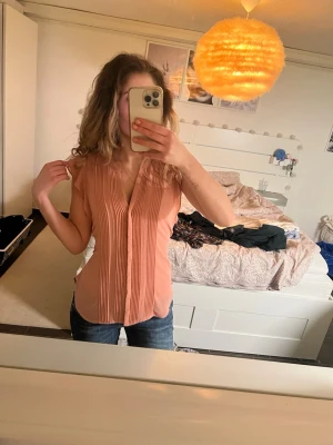 Blus  - Säljer en persikofärgad blus med snygga veck framtill och v-ringning. 