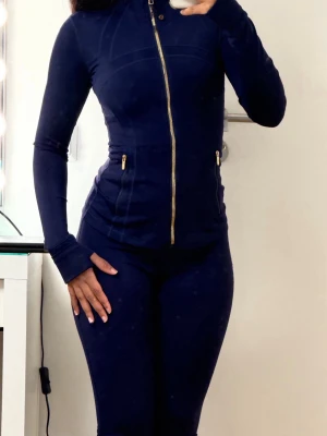 Define jacket navy blue Lululemonset med guldig dragkedja - Snyggt navy blue Lululemonset. Jackan har hel dragkedja i guld, höga fickor med dragkedja och långa ärmar. Byxorna är tighta och högmidjade med lätt utsvängda ben. Säljer settet då byxorna är för små på mig. Det är storlek 2 på både tröjan och byxorna, storleken två passar för både xxxs-xs. Har använt settet 2-3 gånger och settet ser helt ny ut, utan tecken på användning.
