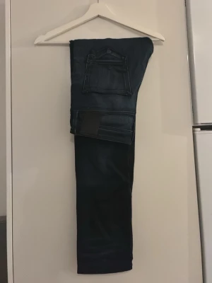 Mörkblå jeans från Jack and Jones  - Snygga mörkblå jeans från Jack and Jones med klassisk femficksmodell och diskret läderpatch bak i midjan. Jeansen har raka ben och är tillverkade i ett mjukt denimtyg som ger en skön passform. Perfekta för dig som gillar stilrena och tidlösa plagg.