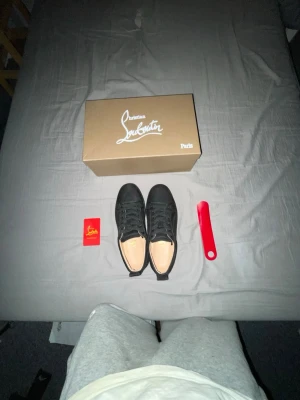 Christian Louboutin svarta sneakers - Svarta sneakers från Christian Louboutin med klassisk låg siluett och ikonisk röd sula med logga. Skorna är i mocka och har svarta skosnören. Kommer med originalkartong och tillbehör. Perfekta för dig som vill sticka ut med exklusiv stil.