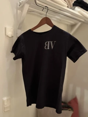 Svart t-shirt med text och strasstenar - Cool svart t-shirt med korta ärmar och texten 'NEED MONEY FOR PORSCHE' i strasstenar på ryggen samt bv logga på fram sida bröst. 