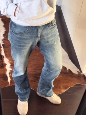 Bootcut jeans med detaljer - Ljusblå jeans med klassisk bootcut-passform. Jeansen har en något sliten look med små detaljer/slitningar och är tillverkade i denim. Perfekta för dig som gillar en avslappnad och tidlös stil. Knappt använda, storlek 32 men passar lite mer som 30. Hör av dig vid intresse😄