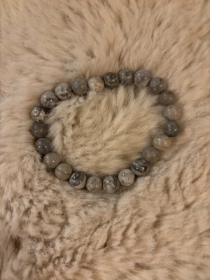 Grått pärlarmband i sten - Snyggt armband med runda pärlor i gråmelerad sten. Pärlorna har olika nyanser av grått och vitt, vilket ger ett unikt och stilrent intryck. Perfekt accessoar för att lyfta din outfit med en naturlig touch.