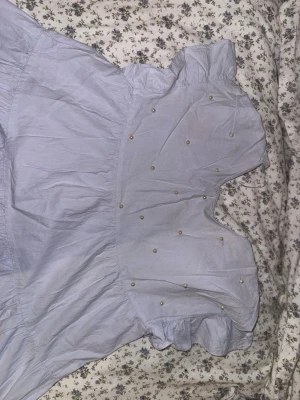 Ljuslila kortklänning med pärlor - Söt ljuslila kortklänning med volangärmar och v-ringning. Klänningen har dekorativa pärlor framtill. Den är i storlek L men är ganska kort och flowy så den passar mindre/större storlekar också 