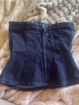 Mörkblå denim korsett-topp - Snygg mörkblå korsett-topp i denim med dragkedja framtill. Axelbandslös modell som sitter tight och markerar midjan. Aldrig använd!