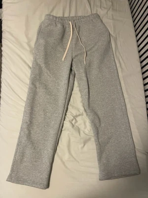 Gråa mjukisbyxor - Säljer ett par klassiska grå mjukisbyxor med vita snören i midjan och raka ben. Byxorna har elastisk midja och är tillverkade i mjukt bomullsmaterial.