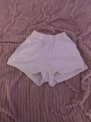 Vita  shorts med resårmidja - Säljer ett par vita shorts med elastisk midja och avslappnad passform. De har en enkel design utan synliga loggor eller detaljer och är perfekta för varma dagar. Materialet känns mjukt och lätt.