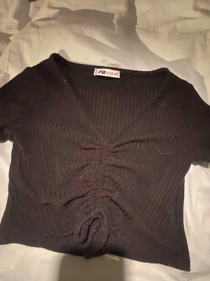 Svart ribbad croppad topp PB Sister - Säljer en svart ribbad croppad topp från PB Sister i storlek XS. Toppen har korta ärmar, v-ringning och snygg snörning framtill som ger en cool detalj. Perfekt till jeans eller kjol för en trendig look.