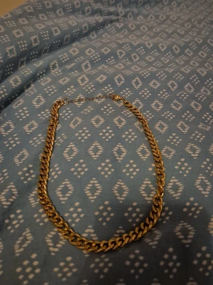 Guldig kedjehalsband - Säljer ett chunky halsband i guldig metall med klassisk kedjelänk. Perfekt för att ge din outfit en extra edge. Justerbar längd med enkel låsning. Passar både till lager på lager eller som statement piece. 
