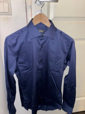Mörkblå skjorta från dressmans - Snygg mörkblå skjorta från Dressmann i slim fit. Skjortan är helt oanvänd har bara testat en gång men den är aldes för liten därav säljer jag den, hör gärna av dig vid frågor, Pris kan diskuteras!!🤩
